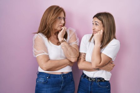 Photo for Hispanic mother and daughter wearing casual white t shirt over pink background looking stressed and nervous with hands on mouth biting nails. anxiety problem. - Royalty Free Image