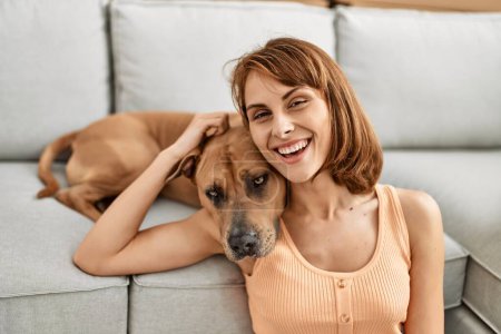Photo for Young caucasian woman hugging dog sitting on floor at home - Royalty Free Image