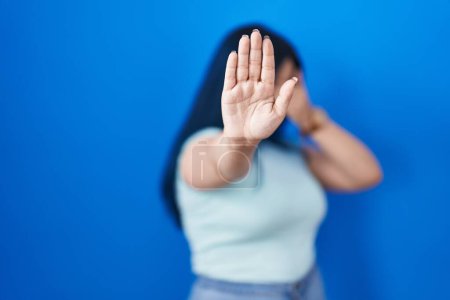 Photo for Young modern girl with blue hair standing over blue background covering eyes with hands and doing stop gesture with sad and fear expression. embarrassed and negative concept. - Royalty Free Image