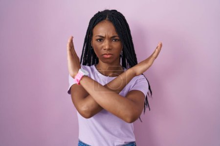 Téléchargez les photos : African american woman with braids standing over pink background rejection expression crossing arms doing negative sign, angry face - en image libre de droit