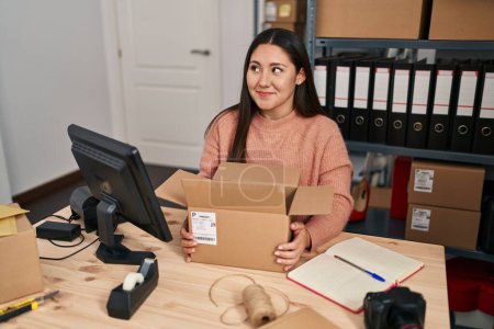 Foto de Mujer latina joven que trabaja en el comercio electrónico de pequeñas empresas sonriendo mirando hacia un lado y mirando hacia otro pensando. - Imagen libre de derechos