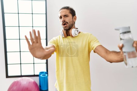 Photo for Young hispanic man wearing sportswear and drinking water at the gym doing stop gesture with hands palms, angry and frustration expression - Royalty Free Image