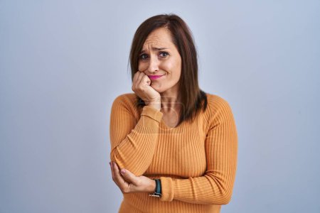 Photo for Middle age brunette woman standing wearing orange sweater looking stressed and nervous with hands on mouth biting nails. anxiety problem. - Royalty Free Image