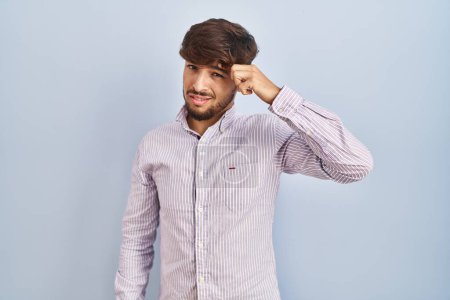 Téléchargez les photos : Homme arabe avec la barbe debout sur fond bleu pointant malheureux de boutons sur le front, infection laide de la tête noire. acné et problème de peau - en image libre de droit
