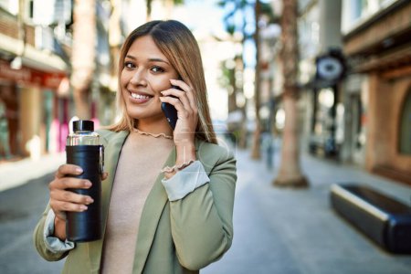 Téléchargez les photos : Jeune femme latine souriant confiant parler sur le smartphone à la rue - en image libre de droit