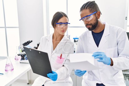 Téléchargez les photos : Man and woman scientist partners reading documents at laboratory - en image libre de droit