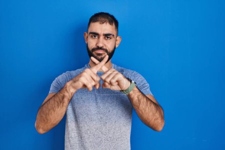 Photo for Middle east man with beard standing over blue background rejection expression crossing fingers doing negative sign - Royalty Free Image