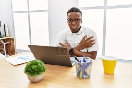 Foto de Young african man working at the office using computer laptop shaking and freezing for winter cold with sad and shock expression on face - Imagen libre de derechos