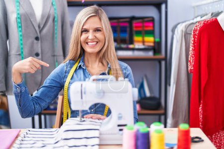 Photo for Blonde woman dressmaker designer using sew machine looking confident with smile on face, pointing oneself with fingers proud and happy. - Royalty Free Image