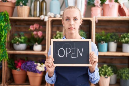 Photo for Young caucasian woman working at florist holding open sign relaxed with serious expression on face. simple and natural looking at the camera. - Royalty Free Image