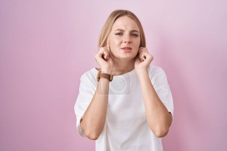 Téléchargez les photos : Young caucasian woman standing over pink background covering ears with fingers with annoyed expression for the noise of loud music. deaf concept. - en image libre de droit