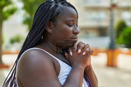 Photo for African american woman praying with closed eyes at park - Royalty Free Image