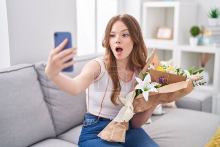 Photo for Caucasian woman holding bouquet of white flowers taking a selfie picture afraid and shocked with surprise and amazed expression, fear and excited face. - Royalty Free Image