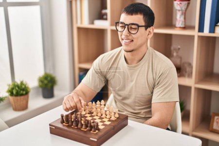 Foto de Joven jugando ajedrez sentado en la mesa en casa - Imagen libre de derechos