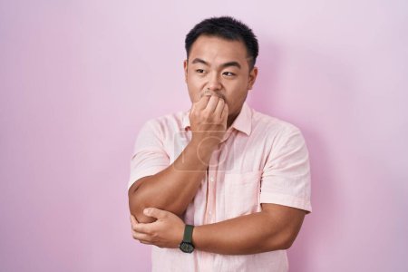 Photo for Chinese young man standing over pink background looking stressed and nervous with hands on mouth biting nails. anxiety problem. - Royalty Free Image