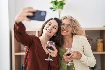 Foto de Dos mujeres madre e hija bebiendo vino hacen selfie por teléfono inteligente en casa - Imagen libre de derechos