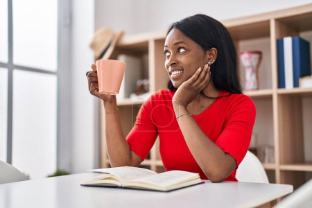 Photo for Young african american woman drinking coffee reading book at home - Royalty Free Image