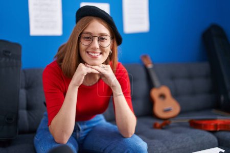 Photo for Young redhead woman artist smiling confident sitting on sofa at music studio - Royalty Free Image