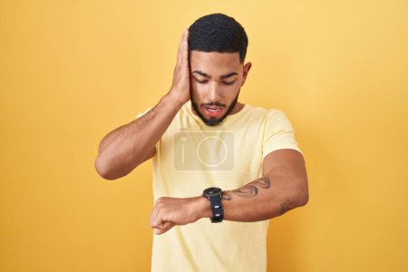 Photo for Young hispanic man standing over yellow background looking at the watch time worried, afraid of getting late - Royalty Free Image