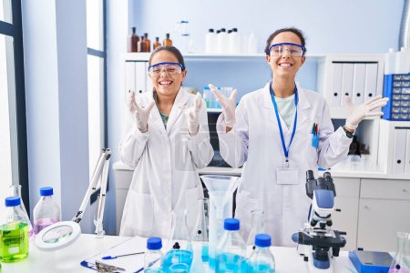 Foto de Young mother and daughter at scientist laboratory celebrating mad and crazy for success with arms raised and closed eyes screaming excited. winner concept - Imagen libre de derechos