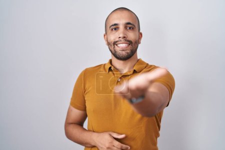 Foto de Hombre hispano con barba de pie sobre fondo blanco sonriente alegre ofreciendo mano de palma dando asistencia y aceptación. - Imagen libre de derechos