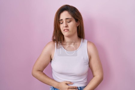Téléchargez les photos : Brunette woman standing over pink background with hand on stomach because indigestion, painful illness feeling unwell. ache concept. - en image libre de droit