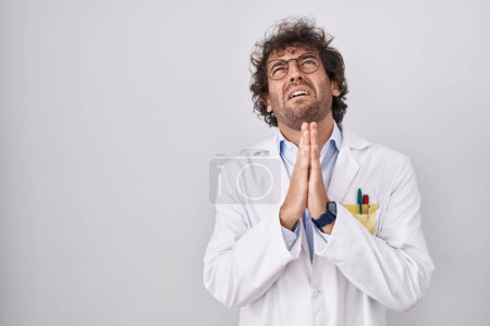 Photo for Hispanic young man wearing doctor uniform begging and praying with hands together with hope expression on face very emotional and worried. begging. - Royalty Free Image
