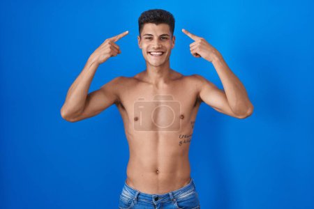 Photo for Young hispanic man standing shirtless over blue background smiling pointing to head with both hands finger, great idea or thought, good memory - Royalty Free Image