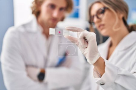 Téléchargez les photos : Man and woman wearing scientist uniform holding sample at laboratory - en image libre de droit