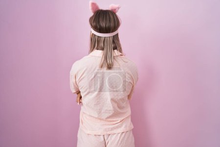Photo for Blonde caucasian woman wearing sleep mask and pajama standing backwards looking away with crossed arms - Royalty Free Image