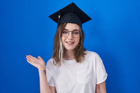 Photo for Blonde caucasian woman wearing graduation cap smiling cheerful presenting and pointing with palm of hand looking at the camera. - Royalty Free Image
