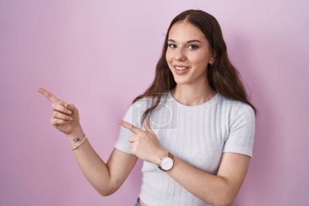 Photo for Young hispanic girl standing over pink background smiling and looking at the camera pointing with two hands and fingers to the side. - Royalty Free Image