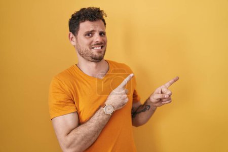 Photo for Young hispanic man standing over yellow background pointing aside worried and nervous with both hands, concerned and surprised expression - Royalty Free Image