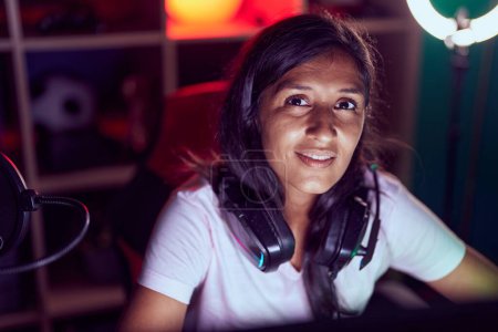 Photo for Young beautiful hispanic woman streamer smiling confident sitting on table at gaming room - Royalty Free Image