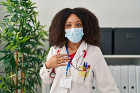 Téléchargez les photos : Young african american doctor woman wearing uniform and medical mask scared and amazed with open mouth for surprise, disbelief face - en image libre de droit