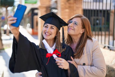 Photo for Mother and daughter making selfie by the smartphone celebrating graduation at university - Royalty Free Image