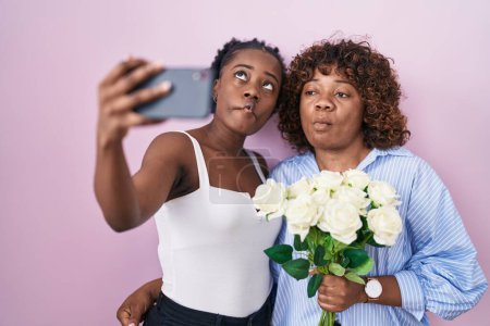 Foto de Dos mujeres africanas tomando una foto selfie con flores haciendo cara de pez con boca y ojos entrecerrados, locas y cómicas. - Imagen libre de derechos