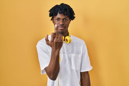 Foto de Young african man with dreadlocks standing over yellow background showing middle finger, impolite and rude fuck off expression - Imagen libre de derechos