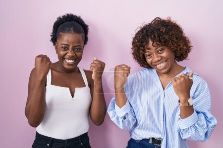 Photo for Two african women standing over pink background very happy and excited doing winner gesture with arms raised, smiling and screaming for success. celebration concept. - Royalty Free Image