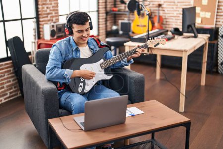 Photo for Young non binary man musician having online electric guitar lesson at music studio - Royalty Free Image