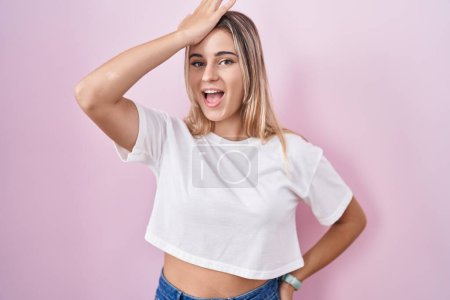 Téléchargez les photos : Young blonde woman standing over pink background surprised with hand on head for mistake, remember error. forgot, bad memory concept. - en image libre de droit