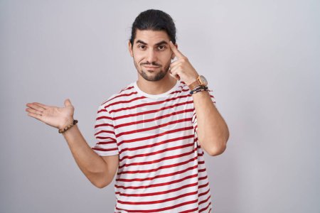 Photo for Hispanic man with long hair standing over isolated background confused and annoyed with open palm showing copy space and pointing finger to forehead. think about it. - Royalty Free Image