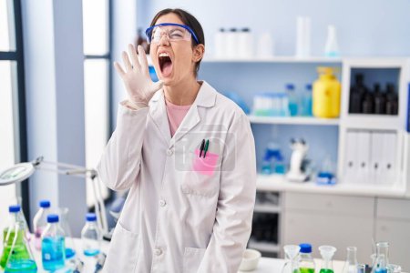 Young brunette woman working at scientist laboratory clueless and confused with open arms, no idea and doubtful face. 