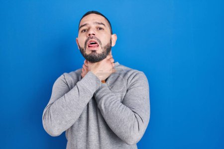 Photo for Hispanic man standing over blue background shouting suffocate because painful strangle. health problem. asphyxiate and suicide concept. - Royalty Free Image