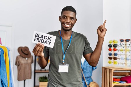 Foto de Joven hombre afroamericano sosteniendo el estandarte del viernes negro en la tienda al por menor sonriendo feliz señalando con la mano y el dedo hacia un lado - Imagen libre de derechos