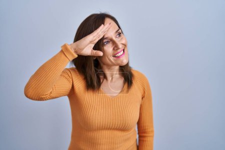 Photo for Middle age brunette woman standing wearing orange sweater very happy and smiling looking far away with hand over head. searching concept. - Royalty Free Image