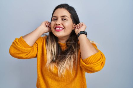 Téléchargez les photos : Young hispanic woman standing over isolated background smiling pulling ears with fingers, funny gesture. audition problem - en image libre de droit