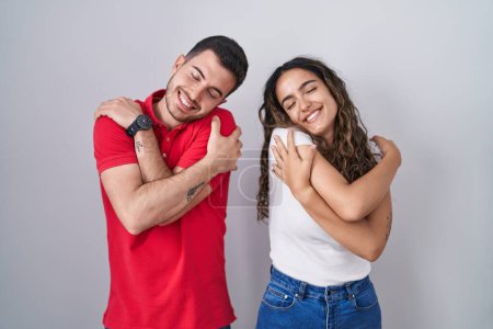 Junges hispanisches Paar, das vor isoliertem Hintergrund steht und sich glücklich und positiv umarmt, selbstbewusst lächelnd. Selbstliebe und Selbstfürsorge 