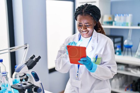 Foto de African american woman scientist smiling confident using touchpad at laboratory - Imagen libre de derechos