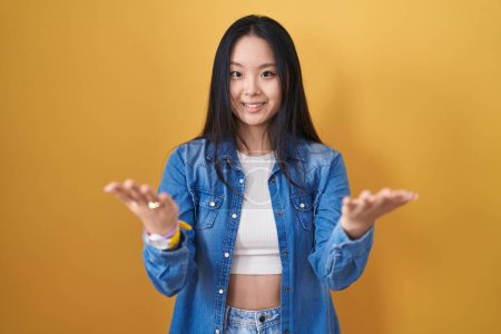 Téléchargez les photos : Young asian woman standing over yellow background smiling cheerful offering hands giving assistance and acceptance. - en image libre de droit